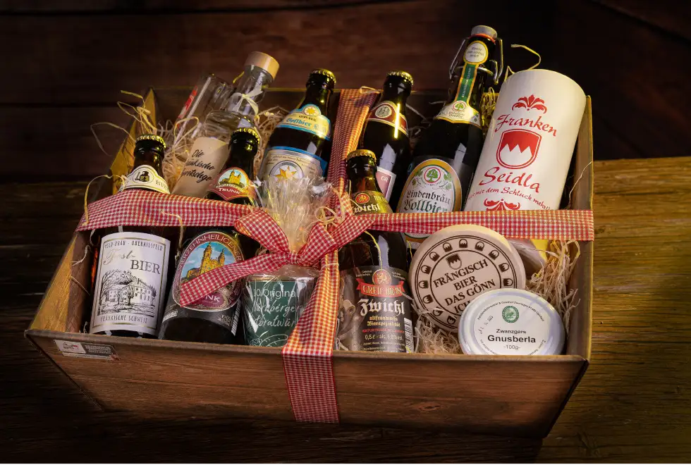 In einer rechteckigen Geschenkverpackung liegen auf Stroh sechs Flaschen Bier daneben ein Bierkrug und ein Schnaps sowie Gnusberla und eine Dose Nürnberger Rostbratwürste